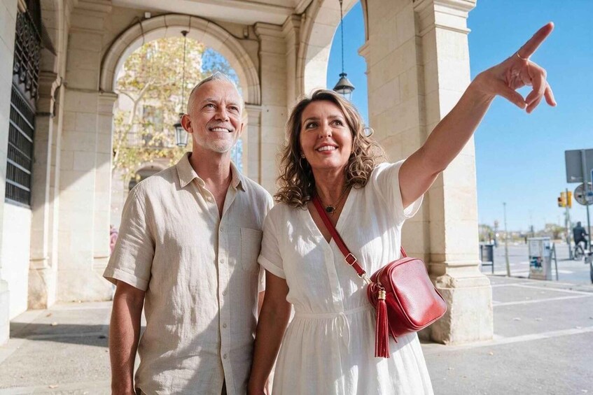 A man and a woman standing in front of a historic archway with a clear blue sky in the background. 2