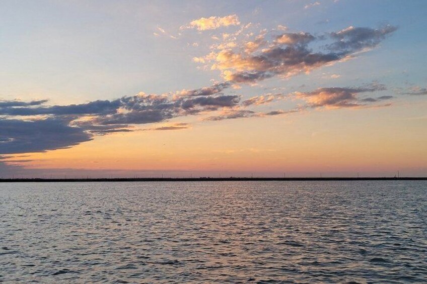 A sunset over a calm sea with a distant shoreline and a line of wind turbines. 3