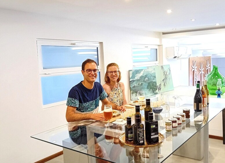 Two people seated at a table with various bottles and glasses, in a room with windows and artwork on the walls. 2