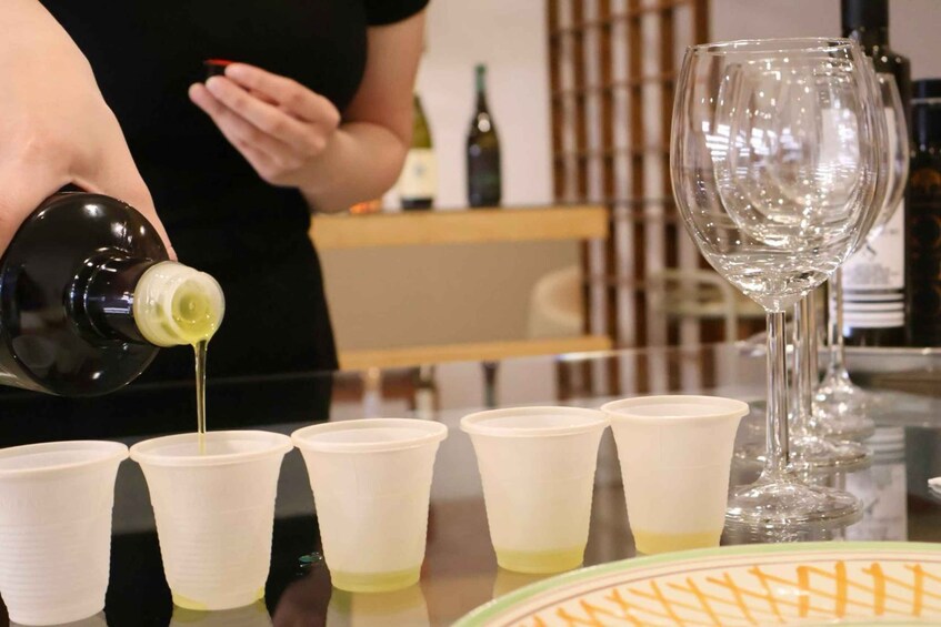 A person pouring a liquid into several white cups on a table. 1