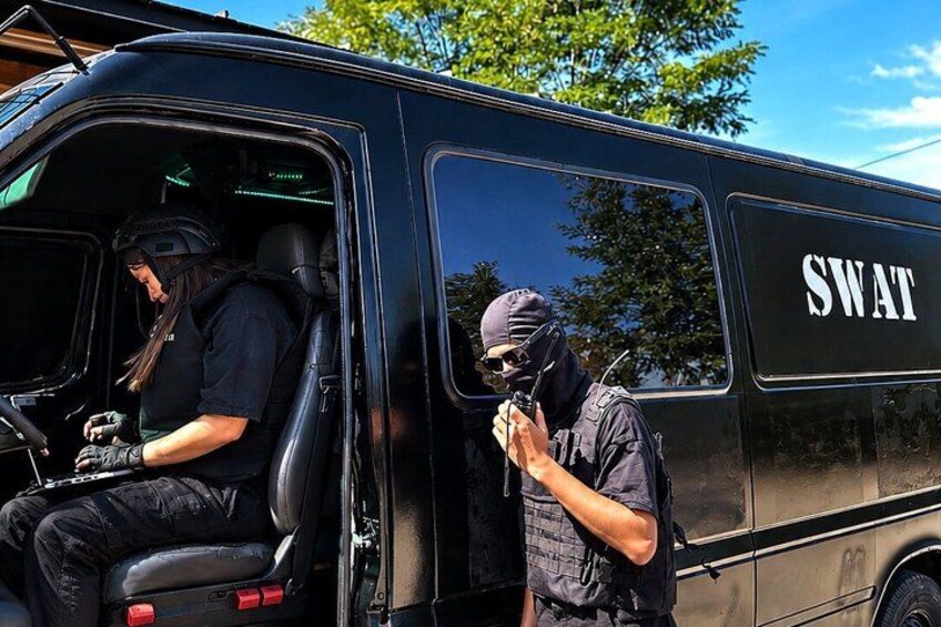 A SWAT van with two officers, one inside and one outside, near a building. 3