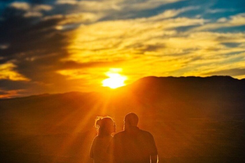 Two people silhouetted against a sunset with a mountain range in the background. 4