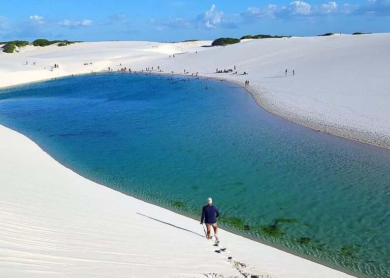 Eine Person geht über eine weiße Sanddüne auf ein klares, blaues Gewässer zu. 4