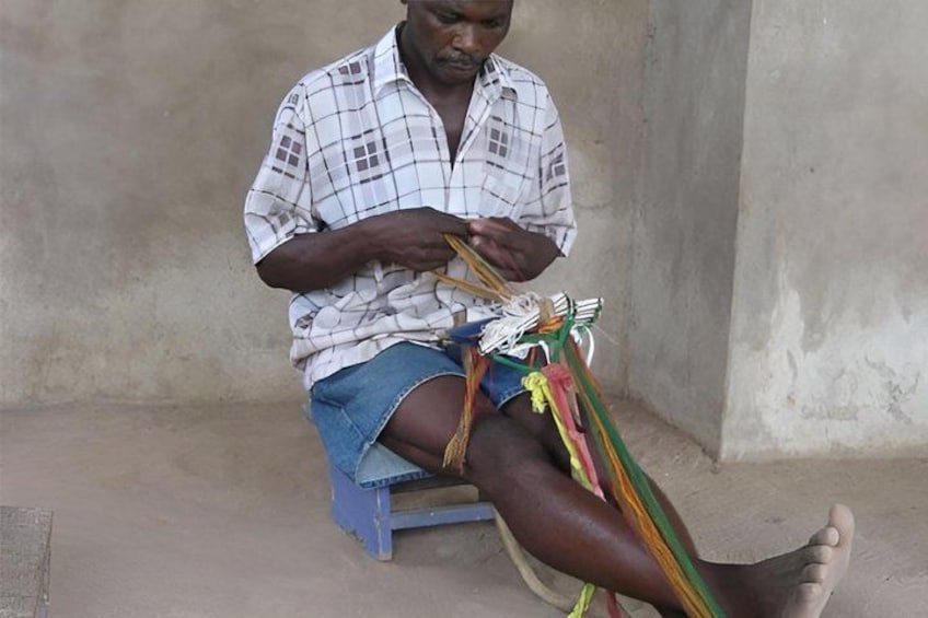A person sitting on a stool, weaving colorful threads. 2