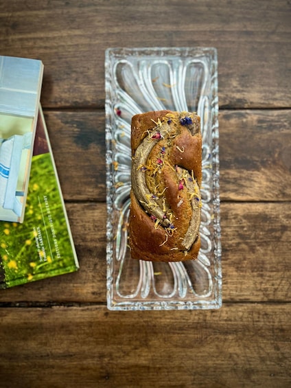 Une miche de pain, décorée de fleurs séchées, posée sur une assiette en verre, elle-même posée sur une table en bois. 2