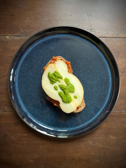 Une tranche de pain garnie de fromage et d’une sauce verte, présentée sur une assiette bleue. 5