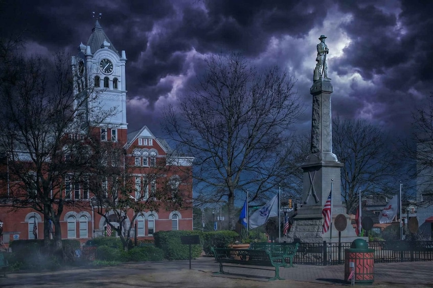 A historic building with a clock tower, a monument, and a park with benches. 1
