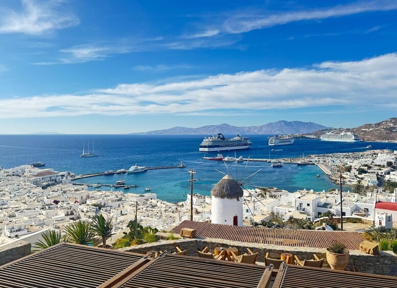 A coastal town with white buildings, a lighthouse, and several cruise ships in the harbor. 1