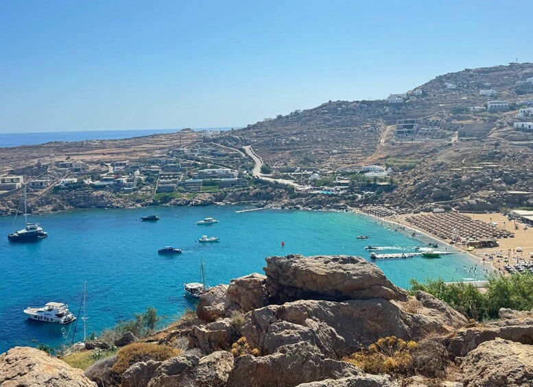 A coastal town with rocky terrain, a clear blue sea, boats, and a beach with umbrellas. 4