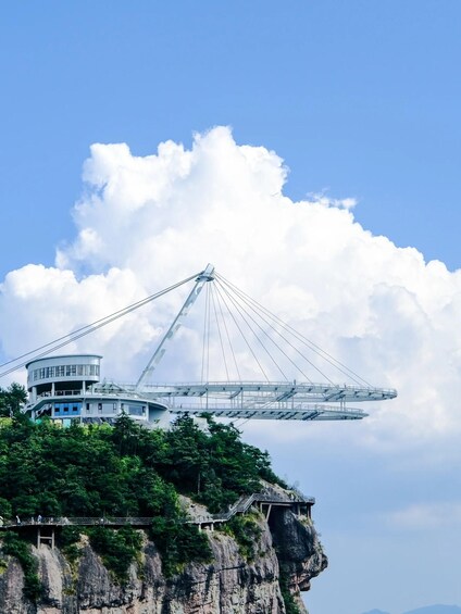 A cable-stayed bridge with a central tower and a building on a cliff. 3