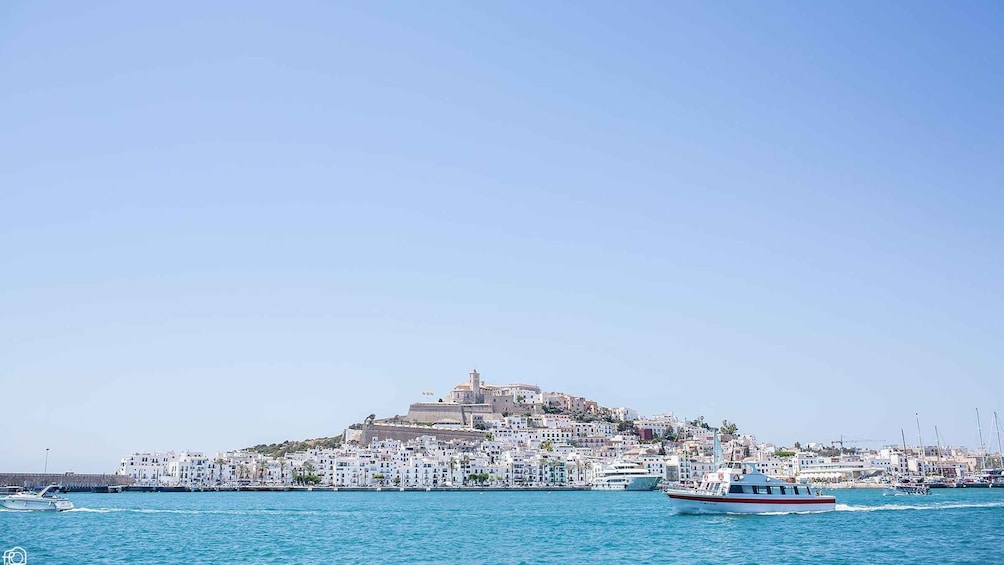A coastal town with a prominent hilltop fortress, a marina with boats, and a clear blue sky. 1