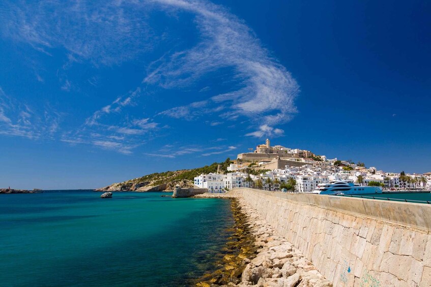 A coastal town with a prominent castle on a hill, clear blue skies, and calm turquoise waters. 2