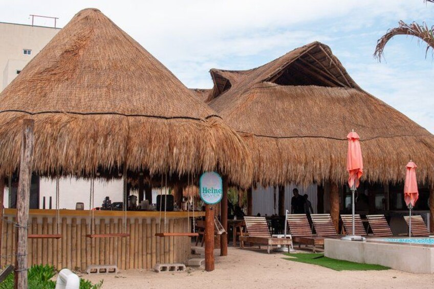 A beachside bar with thatched roofs, a sign for Heineken, and lounge chairs. 4