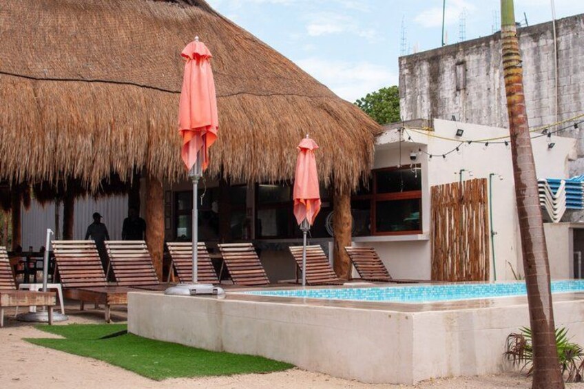 A pool area with lounge chairs and a thatched-roof building. 3