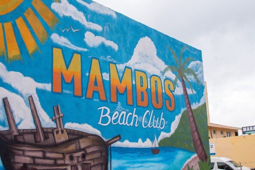 A mural of a beach scene with a ship, palm trees, and the text 'MAMBOS Beach Club'. 2