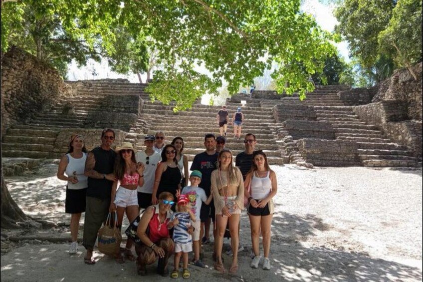 A group of people posing in front of ancient stone steps with trees overhead. 1