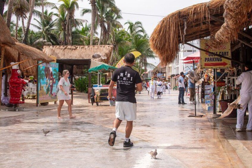 A wet street with people walking, a thatched-roof structure, and a sign for golf cart parking. 5