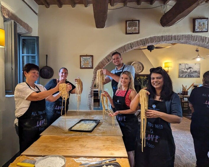 Personas preparando pasta en una cocina rústica con vigas de madera a la vista y un arco de piedra. 2