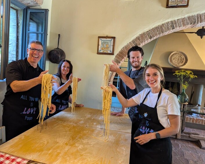 Cuatro personas preparando pasta en una cocina con un arco de piedra rústico y una mesa de madera. 4