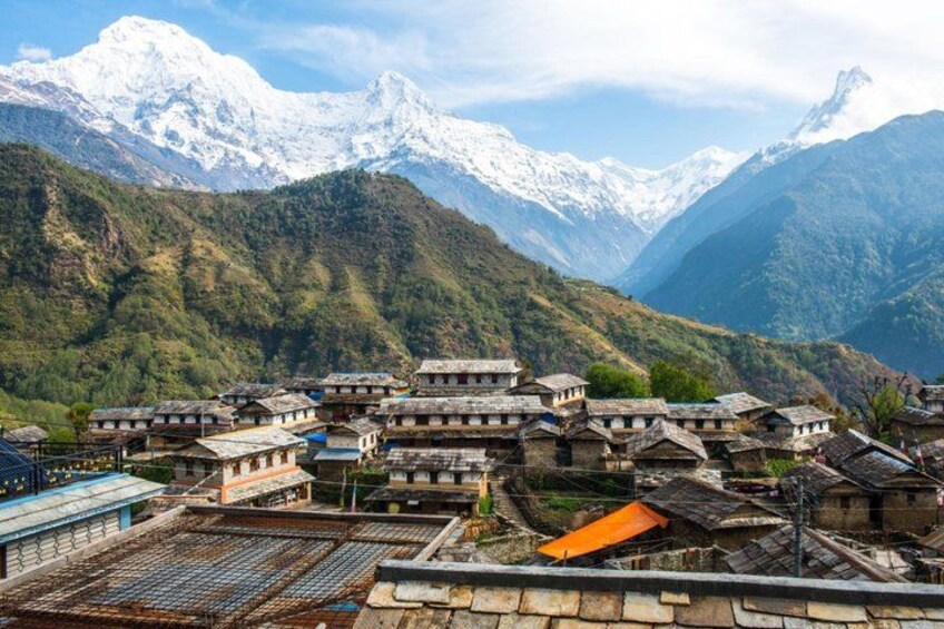 A village with traditional houses, a railway track, and snow-capped mountains in the background. 1