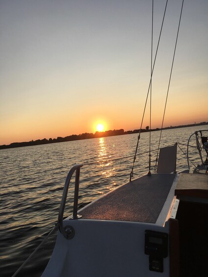 A sunset over a calm body of water with a boat's deck and railing in the foreground. 5