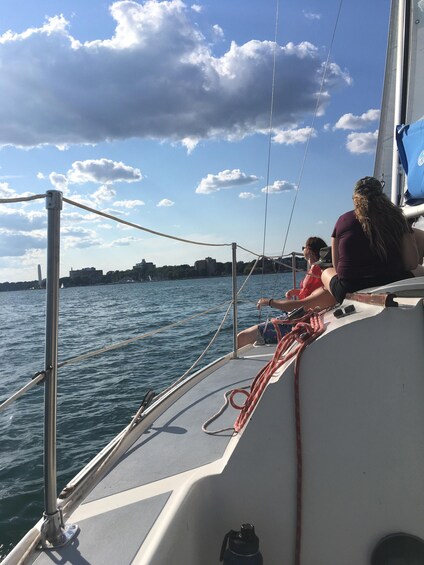 A sailboat with two people on deck, a city skyline in the background, and a partly cloudy sky. 4