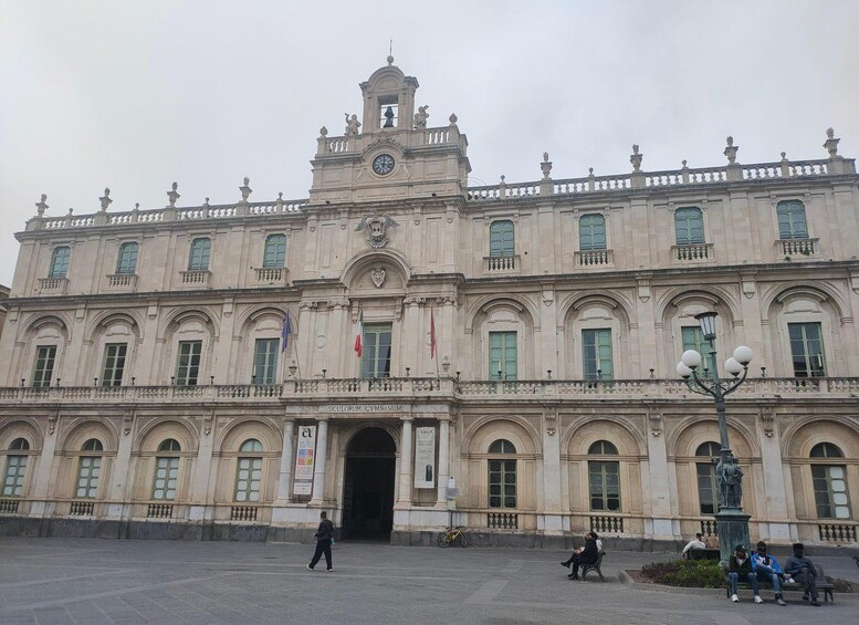 A large historic building with a clock tower, arched windows, and a central entrance. 1