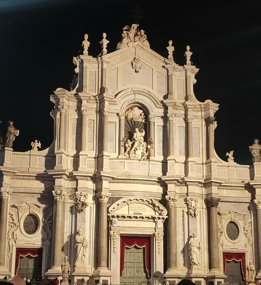 A grand, ornate building with multiple statues and columns, featuring a central arched window and red doors. 2