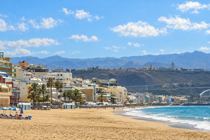 A beach with buildings, palm trees, and mountains in the background. 5
