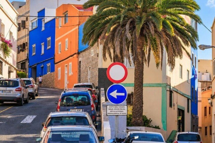 A narrow street with parked cars, colorful buildings, and a palm tree. 2