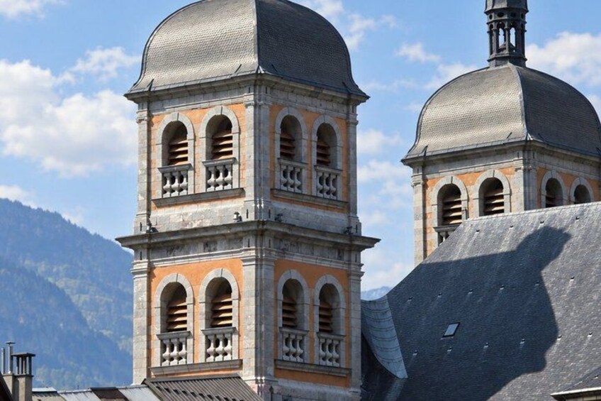 A bell tower with arched windows and a dome, set against a mountainous backdrop. 2