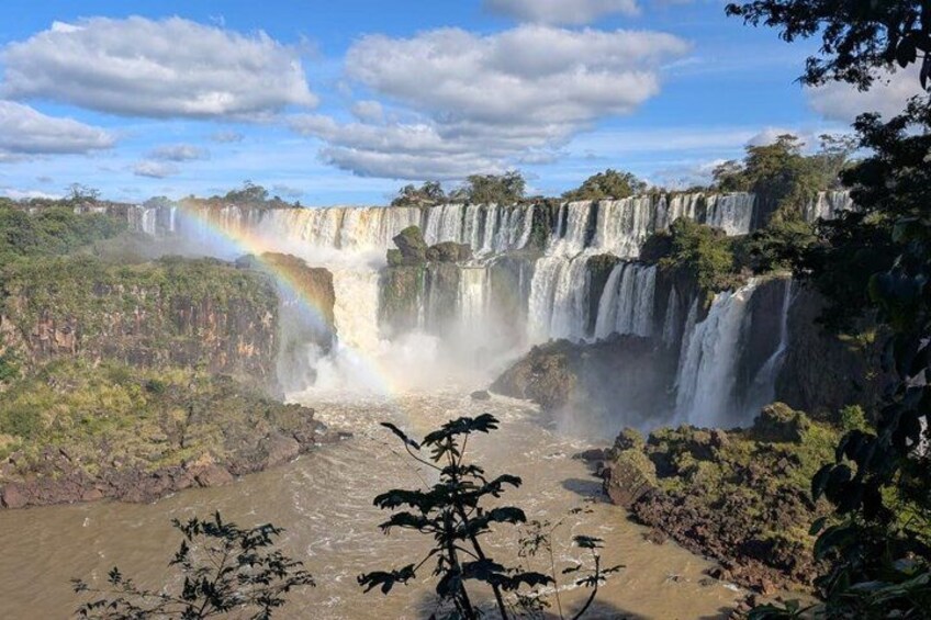 A multi-tiered waterfall with a rainbow, surrounded by dense vegetation. 1