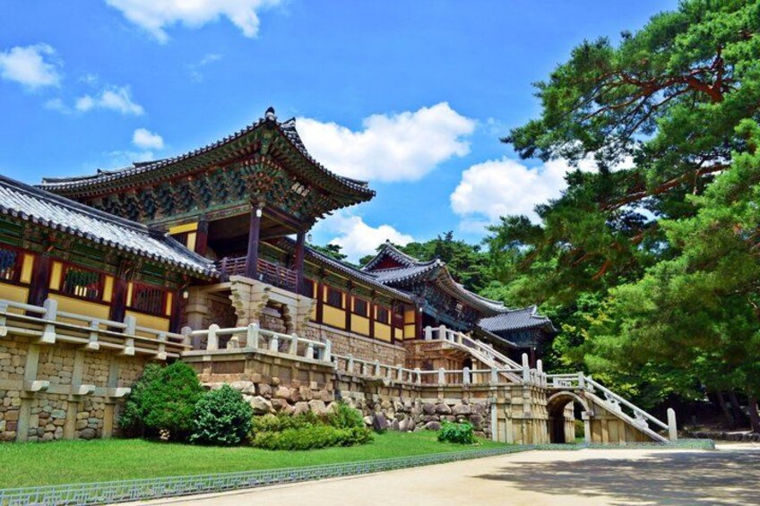 Un palacio coreano tradicional con arquitectura ornamentada, un puente de piedra y abundante vegetación. 1