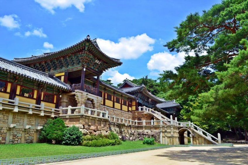 A traditional Korean palace with ornate architecture, a stone bridge, and lush greenery. 1