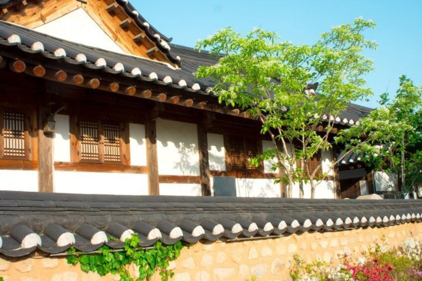 A traditional Korean building with wooden beams, tiled roof, and a stone wall with plants. 3