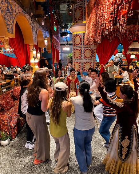 A group of people dancing in a decorated indoor venue with traditional patterns and red curtains. 3