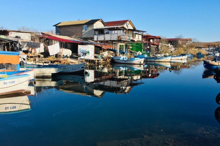 A calm harbor with boats, a house with a red roof, and a clear blue sky. 3