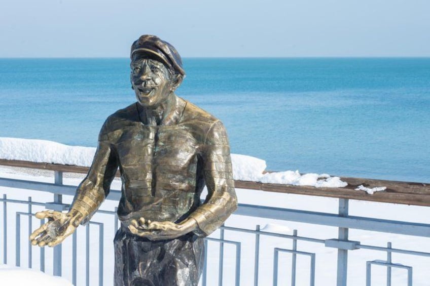 A bronze statue of a man in a hat and jacket by the seaside. 1