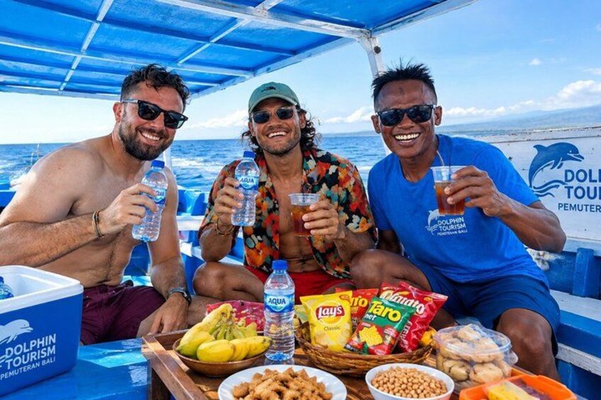 Three people on a boat with food and drinks, a dolphin logo, and a tropical setting. 2