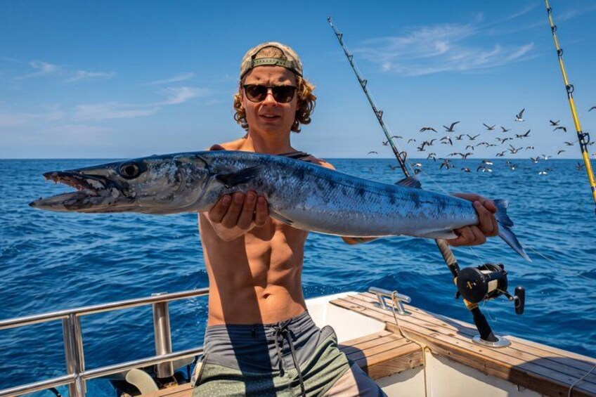 A person holding a large fish on a boat with the ocean and birds in the background. 3