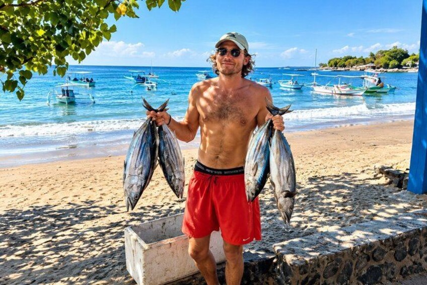 A man holding fish on a beach with boats in the background. 4