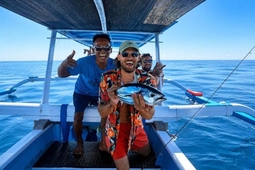 A boat with two people holding a fish, a clear blue sea, and a person giving a thumbs-up. 1