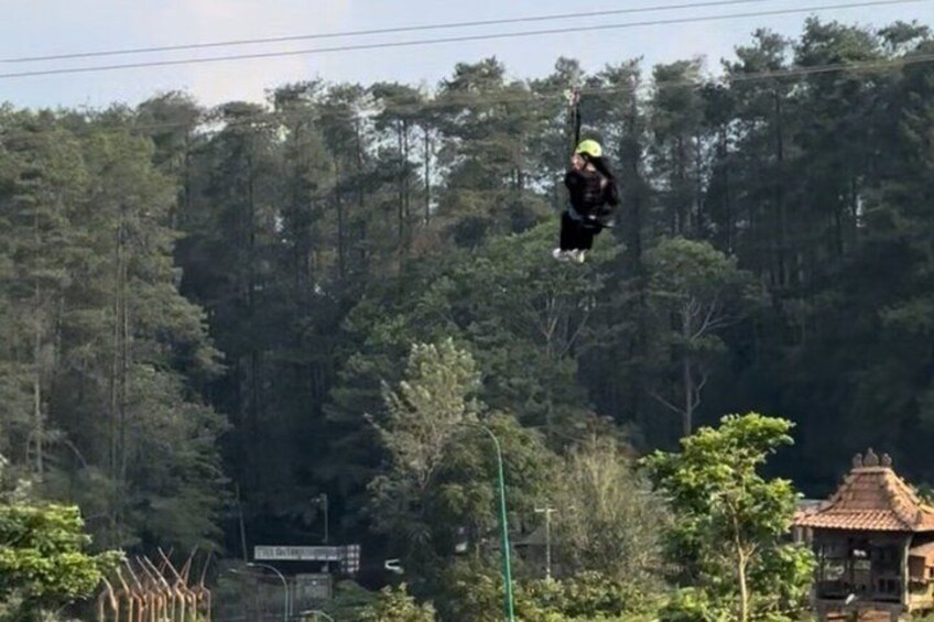 A person bungee jumping with a forest and a traditional building in the background. 2