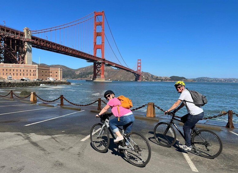 Two cyclists on a paved path with a red bridge in the background. 2