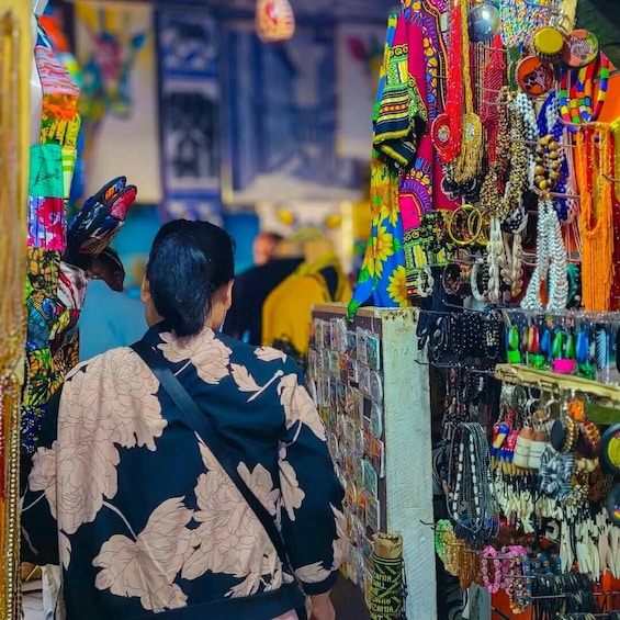 A person walking through a market with colorful jewelry and clothing stalls. 5