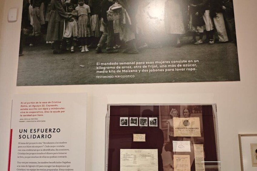 A historical photograph of women carrying a load, with a display case and informational text below. 2