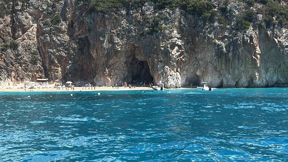 Une plage côtière aux eaux d’un bleu limpide, bordée d’une falaise rocheuse et abritant l’entrée d’une grotte. 4
