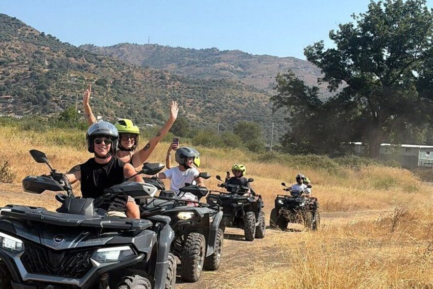 Four people on ATVs in a grassy field with hills in the background. 2