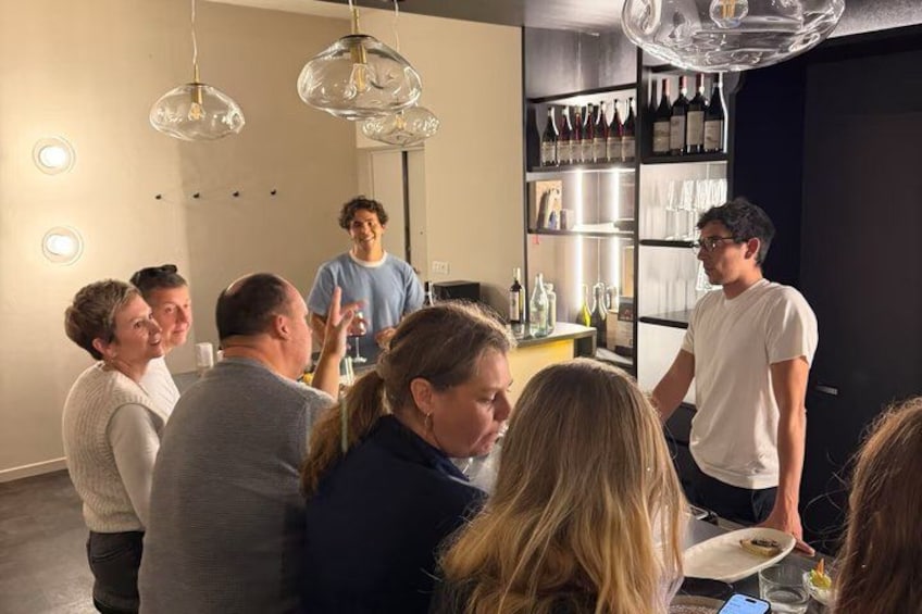 A group of people in a modern interior with pendant lighting, a wine rack, and a person standing in the background. 1