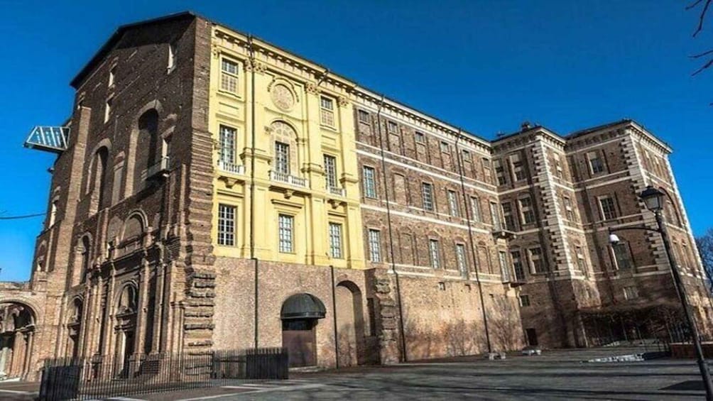 A historic building with yellow and brown facades, large windows, and a prominent entrance. 1